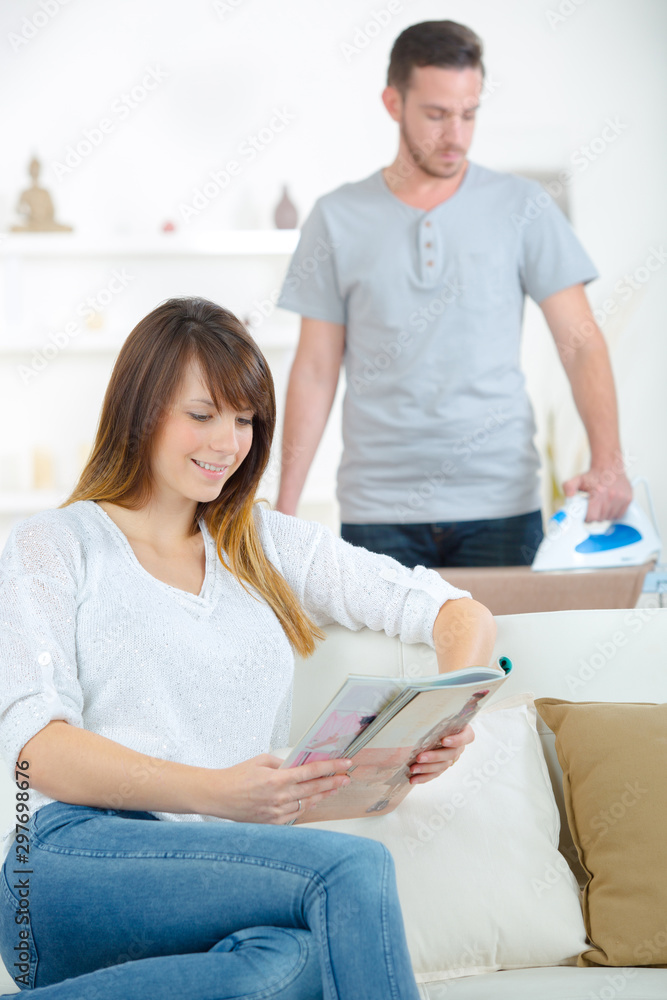 man doing some ironing while girlfriend is reading man doing some ironing while girlfriend is reading