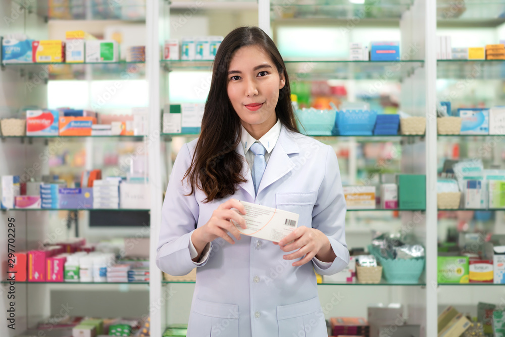 Asian young woman pharmacist with a lovely friendly smile holding medicinebox and looking at camera in the pharmacy drugstore. Medicine, pharmaceutics, health care and people concept.