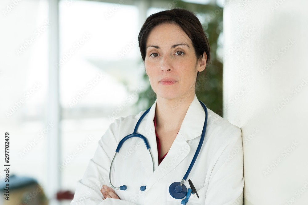 serious female doctor with crossed hands near window serious female doctor with crossed hands near window