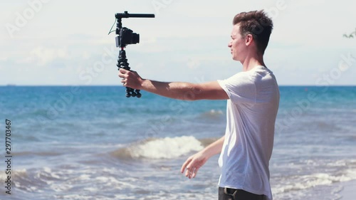 Young male vlogger filming travel story on the beach. photo