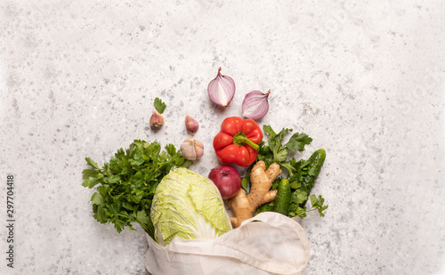 Eco-friendly bag for products with vegetables: Bulgarian red pepper, Pikin cabbage, cucumbers, ginger, garlic, onions, parsley, greens on a concrete background with copy space. Save the planet