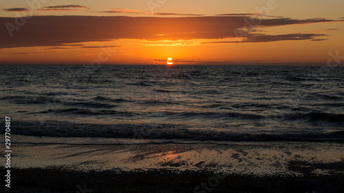 Orange sun highlights storm clouds on a warm evening on a Gulf Coast Florida beach.