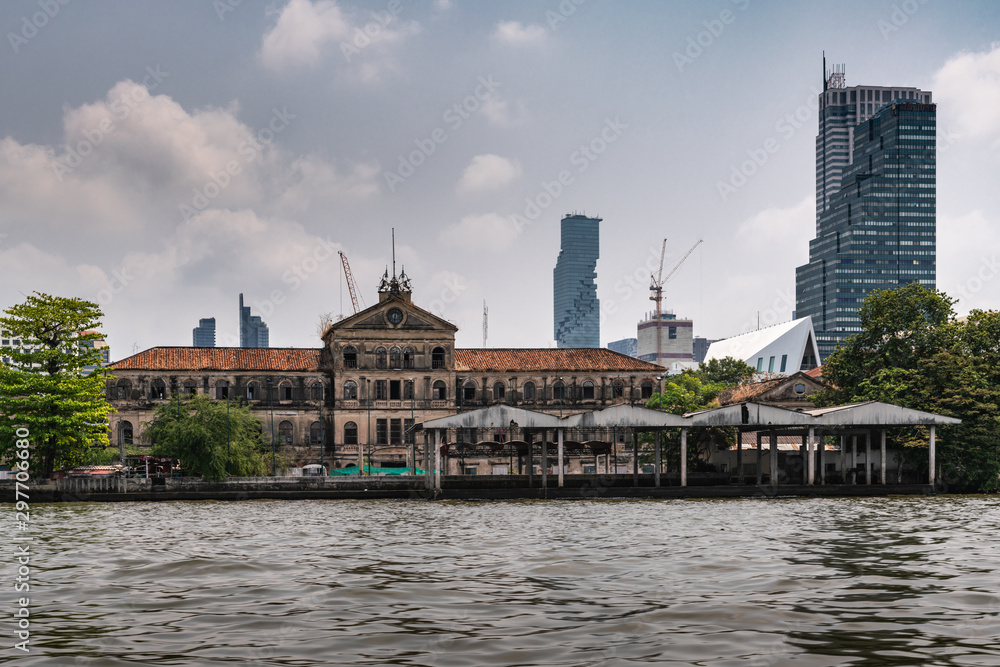 Bangkok city, Thailand - March 17, 2019: Chao Phraya River. Skyscrapers of offices and hotels around ruin of Old Customs House at quay. Silver sky with cloudscape. King Power MahaNakho skyscraper in b