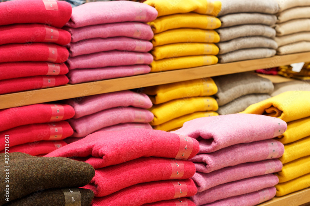 Piles of multicolored sweater on the shelves in store women's clothing