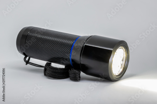 Obraz na płótnie A black metal flashlight on its side, powered on, isolated on a white background. w salonie