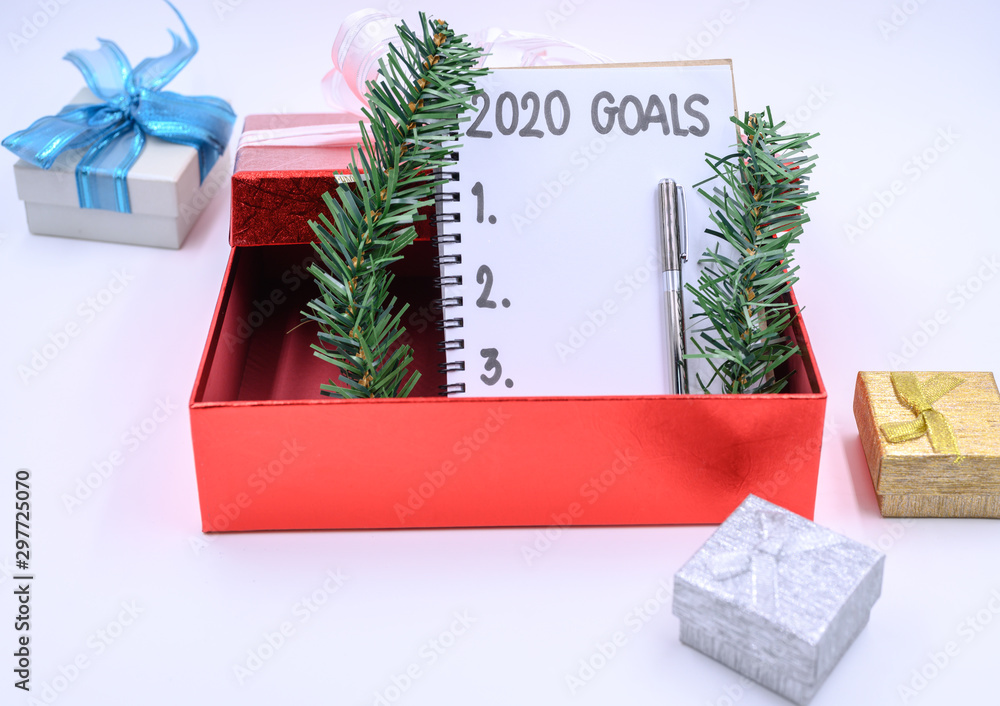 Red empty gift box with list of goals for 2020 written in notepad paper  with copy space for your goals. decorated with christmas decorations on the  white table background. foto de Stock