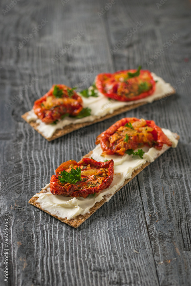 Two bread toast with cream cheese and sun-dried tomatoes on a wooden table.