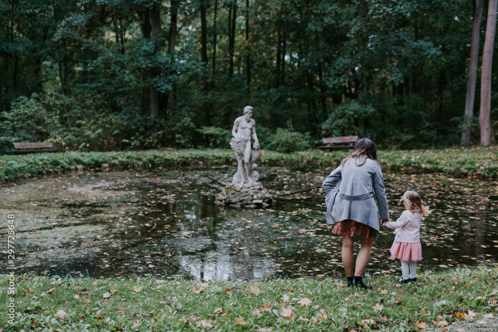 Fototapeta premium Beautiful little looking at the statue in the pond. Sunny day. Autumn day.