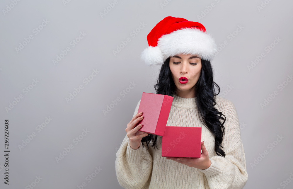 Young woman with santa hat opening a Christmas gift box on a gray background Young woman with santa hat opening a Christmas gift box on a gray background