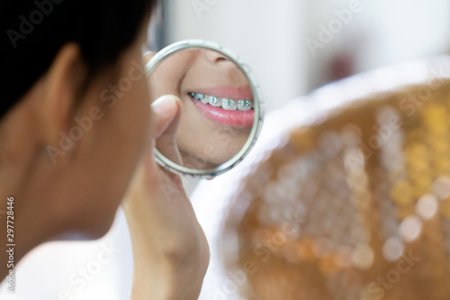 Girl with braces teeth looking to the mirror cleaning her teeths