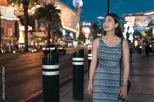 Beautiful young woman traveler walking in night city in las vegas nevada. cheerful lady tourist sightseeing around urban with nightlife. female in dress smiling relax on busy modern area in usa.