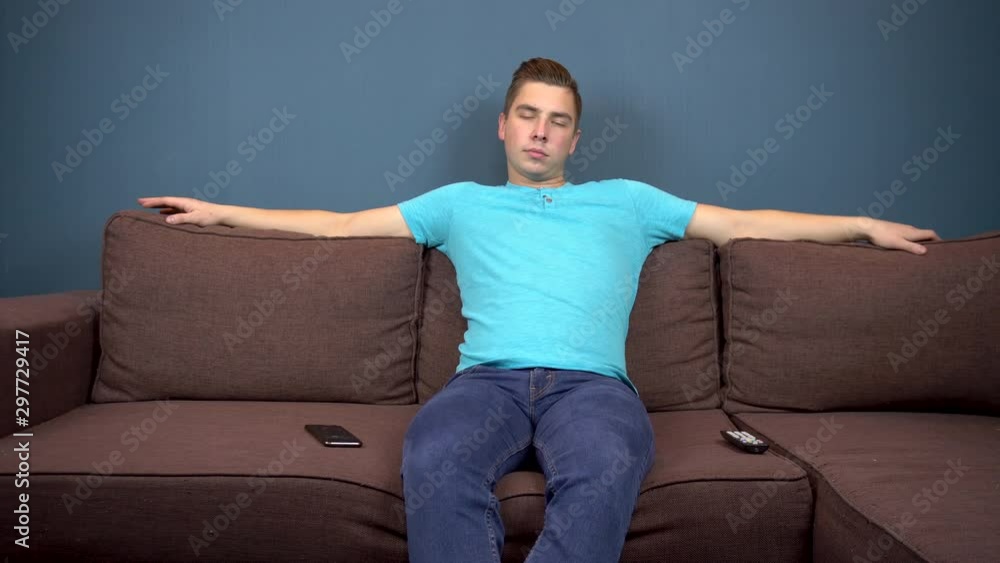 A young man sits on a sofa and watches TV. The view from the TV. Looking at the camera A young man sits on a sofa and watches TV. The view from the TV. Looking at the camera
