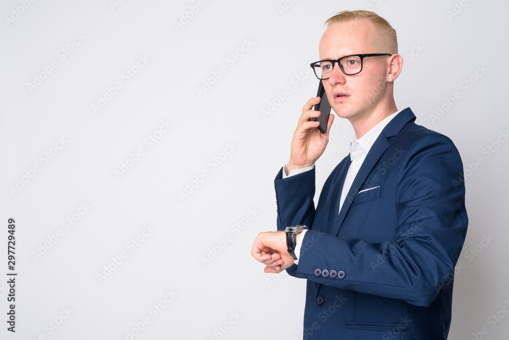 Young blonde businessman in suit talking on the phone and checking time Young blonde businessman in suit talking on the phone and checking time