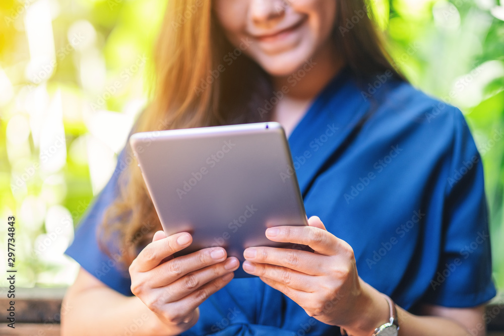 Closeup image of a beautiful woman holding and using tablet pc while sitting in the garden Closeup image of a beautiful woman holding and using tablet pc while sitting in the garden