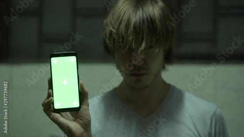 Face of crazy disheveled young man showing phone and laughing in dark creepy room
