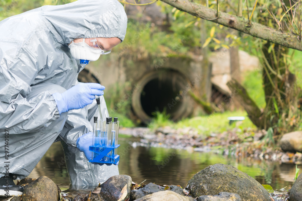 a man in special protective clothing holds a set of test tubes in front of him and does a water analysis a man in special protective clothing holds a set of test tubes in front of him and does a water analysis