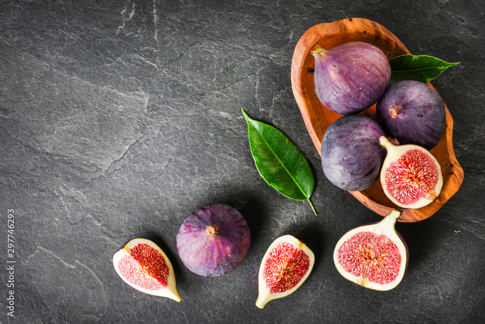 Fresh figs in rustic wood bowl top view. Cut fig fruit on dark stone table or black background with copy space. Fresh figs in rustic wood bowl top view. Cut fig fruit on dark stone table or black background with copy space.