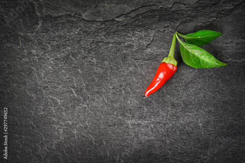 One red hot pepper on dark stone table. Chili small spice ingerdients and green leaves on black background top view and copy space.