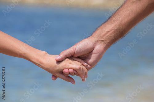 The man and the woman keep for hands. Against the sea water on the beach, close up