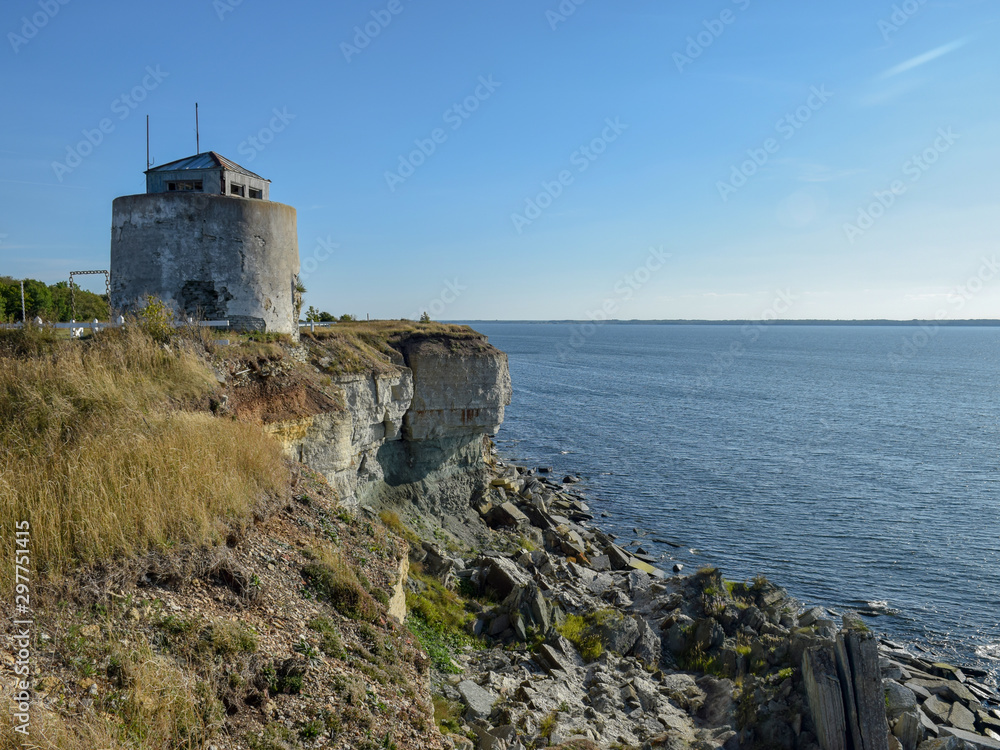 old stone building on a steep sea shore with blue sea and sky in the background