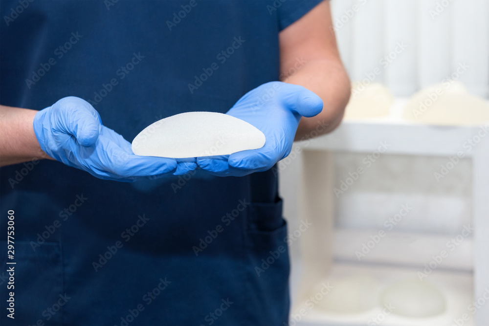 Fototapeta premium Doctor holding silicone implant for breast augmentation, space for text. Plastic surgeon hands holding silicon breast implants. Cosmetic surgery
