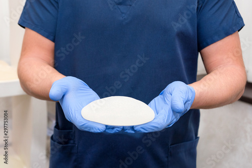 Doctor holding silicone implant for breast augmentation, space for text. Plastic surgeon hands holding silicon breast implants. Cosmetic surgery photo