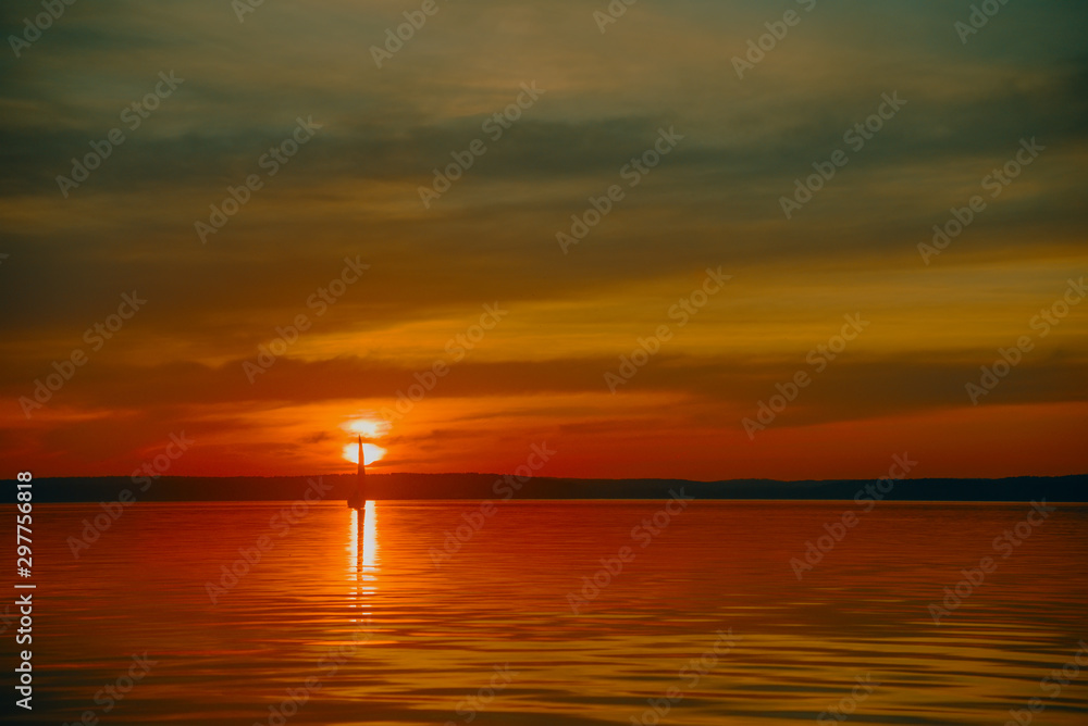 Sailing boat floats on the lake at sunset.