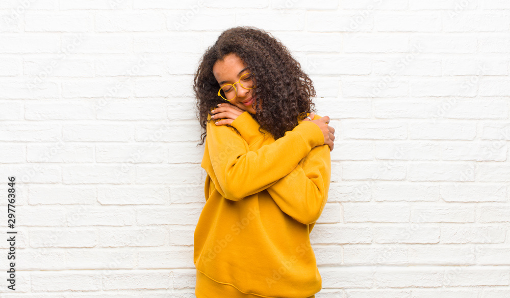 young black woman feeling in love, smiling, cuddling and hugging self, staying single, being selfish and egocentric against brick wall - obrazy, fototapety, plakaty 