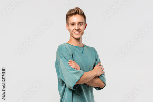 Smiling young man in a green tee holds hands folded isolated over grey background.