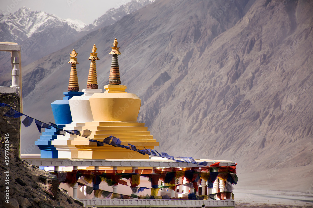 Colorful three stupa or chedi in Maitreya Buddha statue and Diskit Monastery perched against the hills at nubra valley village at Leh Ladakh in Jammu and Kashmir, India