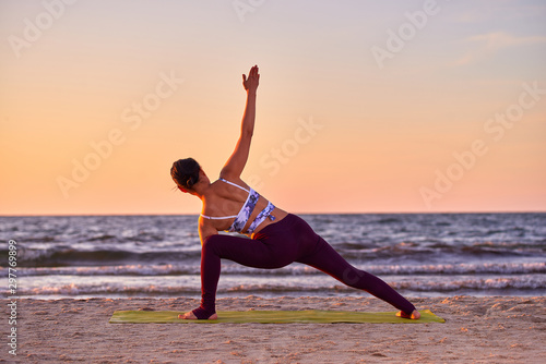 Young woman doing yoga at sunset by the sea