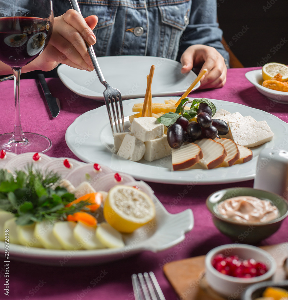 woman taking cheese from cheese plate with smoked, white, gouda, feta cheese, olive woman taking cheese from cheese plate with smoked, white, gouda, feta cheese, olive