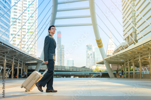 Business man walking with suitcase in city.
