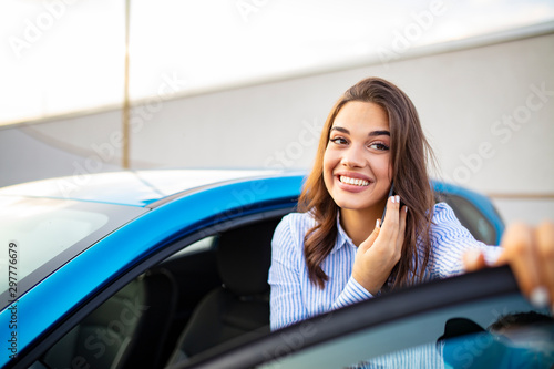Woman using mobile phone near car. Young beautiful woman looking aside talking on cellphone standing near car on city street. Young woman talking on phone near car outdoors