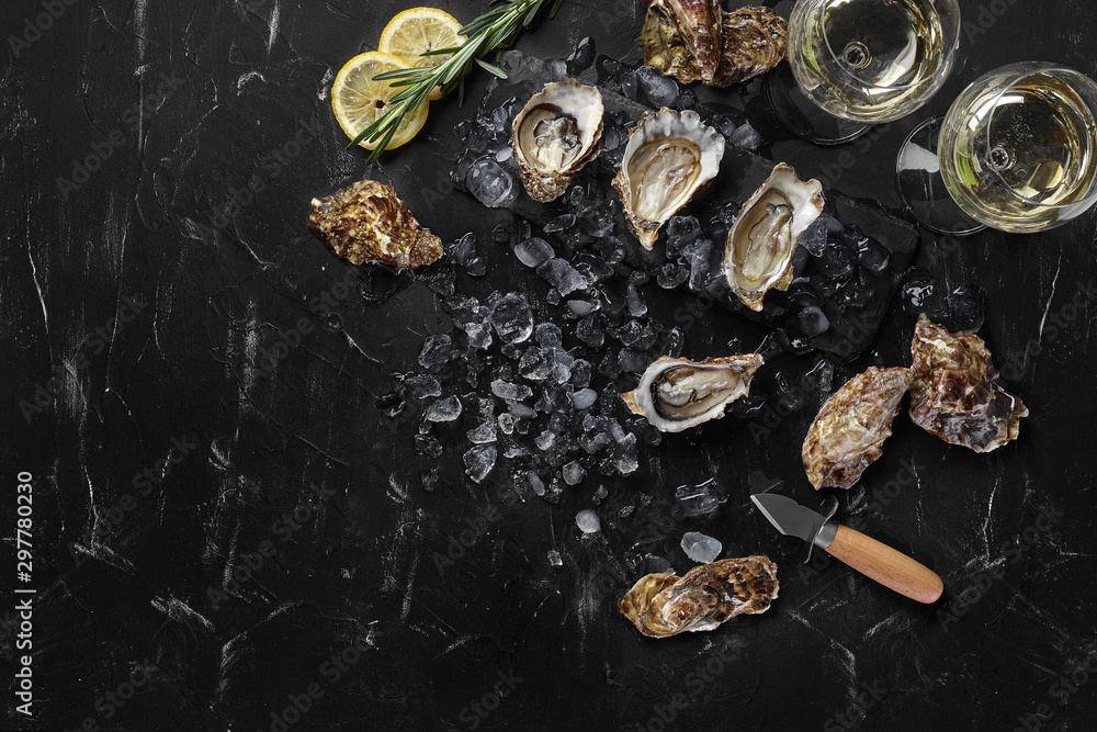 Fresh opened oysters, ice, lemon on a rectangle slate and champagne are on a black stone textured background. Top view with copy space. Close-up.