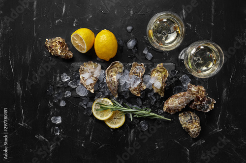 Fresh closed oysters, ice, lemon on a rectangle slate and champagne are on a black stone textured background. Top view with copy space. Close-up.
