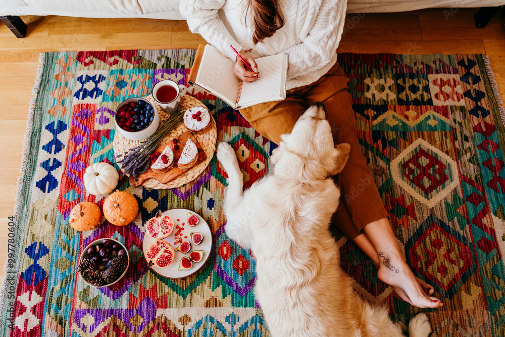 Fototapeta premium beautiful woman enjoying a cup of coffee during healthy breakfast at home. Writing on notebook. Adorable golden retriever dog besides. Lifestyle indoors
