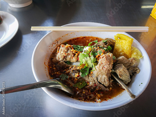 Hot and Sour soup Pork Bone Yellow Noodle in white cup. Use chopsticks and a spoon for eatting.