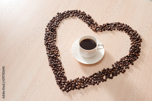 Coffee cup with roasted beans shapes love around on wood background