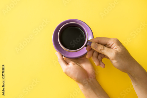 Hand holding the cup of coffee on the yellow background