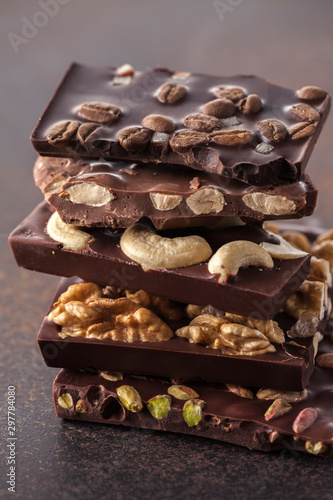 chocolate bar pieces with pistachios, cashew nuts, coffee beans, filbert and walnuts on brown background.