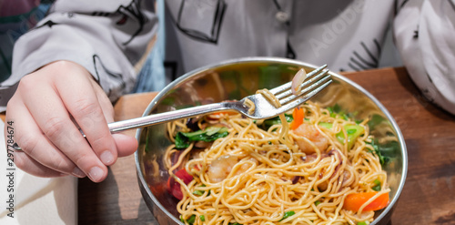 Big bowl of Golden fried noodles with vegetables and shrimp, Asian cuisine. Eating kid: in a small hand close-up of a fork with a piece of food