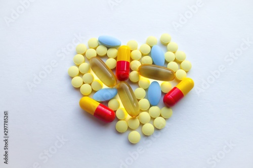 A lot of colorful tablets are laid out in the form of a heart on the background of a white textured rough sheet of paper with space for text