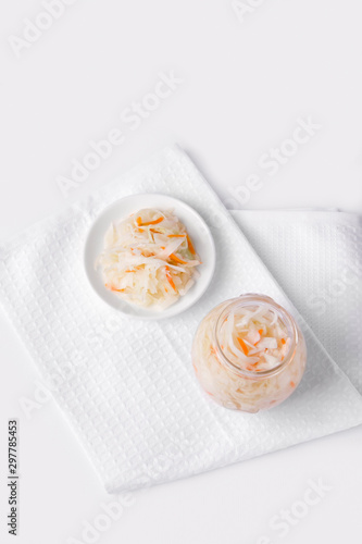 Pickled cabbage and carrot on a plate, next to a jar of marinade. Fermented foods. White background. Copy space