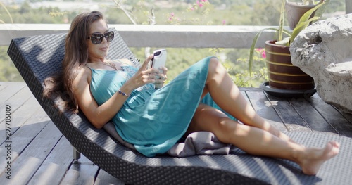 Attractive woman with smartphone resting on chaise lounge Fototapeta
