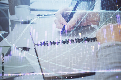 Hand taking notes in notepad. Forex chart holograms in front. Concept of research. Double exposure