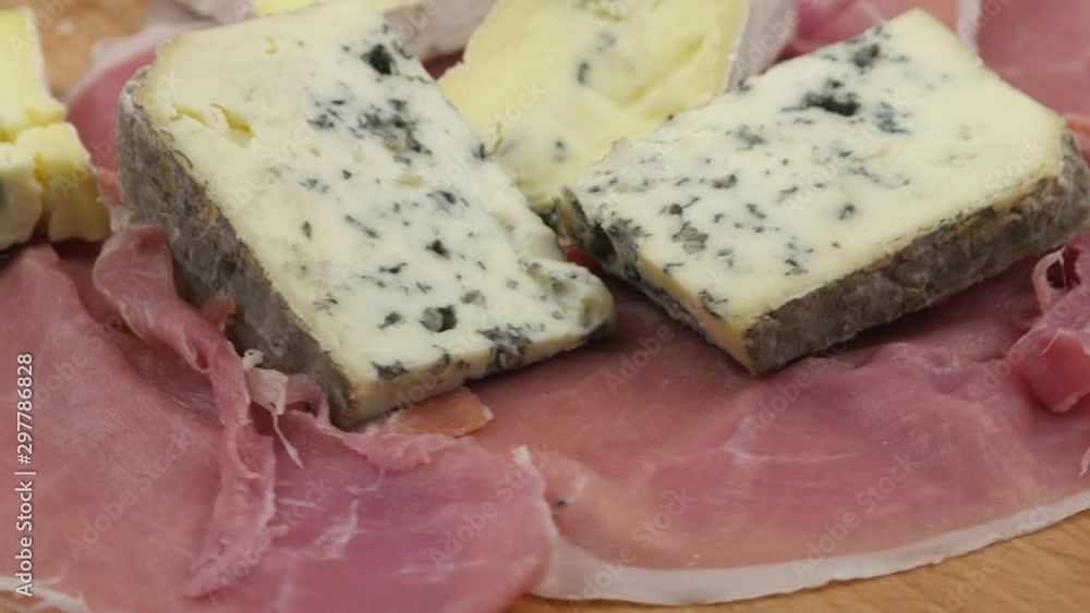 Sliced jamon and pieces of blue cheese laid out on a wooden board, background Sliced jamon and pieces of blue cheese laid out on a wooden board, background