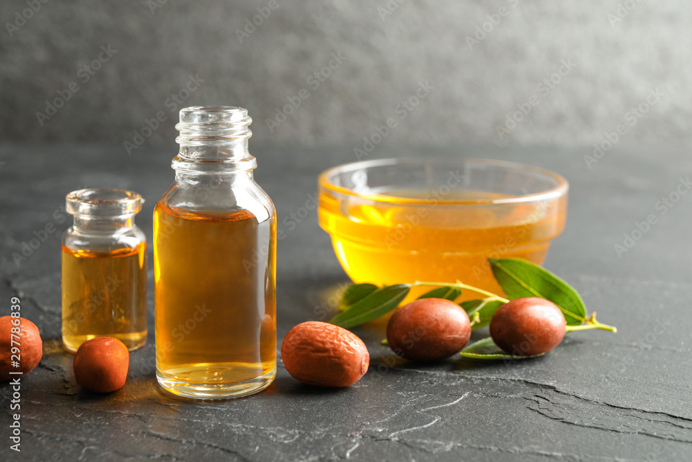 Jojoba oil and seeds on dark grey table Jojoba oil and seeds on dark grey table