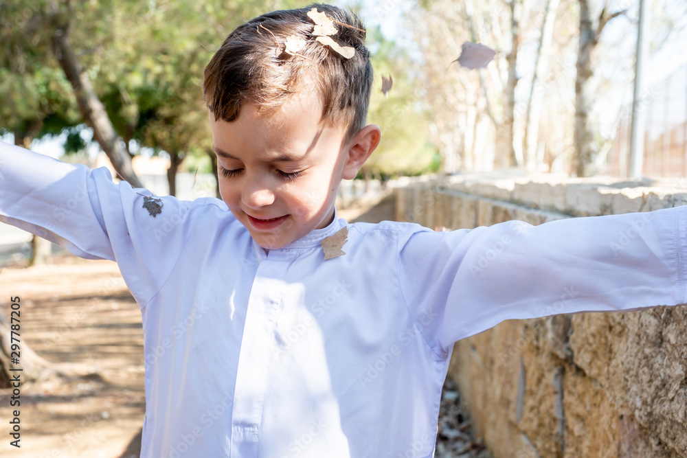 Happy arabic boy enjoying playing with dried leaves outside in th park Happy arabic boy enjoying playing with dried leaves outside in th park