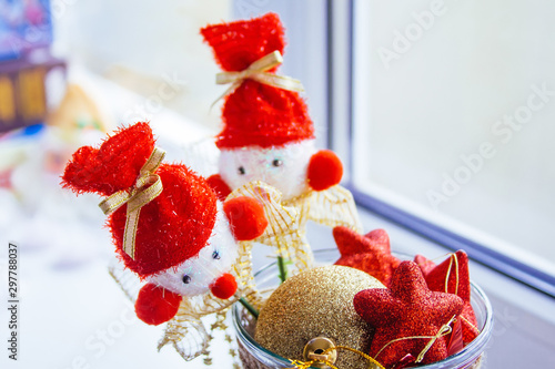 A vase stands at the window filled with red and yellow Christmas tree toys. Two snowmen on sticks are on top.